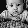 baby, black_and_white, close_up, portrait, infant, face, eyes, blanket, texture, clothing, curious, expression, head, young_child, indoors, soft_light, monochrome, sitting, person, cute