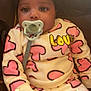 Tyla is registered to the contest to win money with this photo: baby, pacifier, headband, bow, heart_pattern, love_text, infant, clothing, cute, child, sitting, indoors, soft_lighting, face, expression, pink, white, adorable, young_child, portrait
