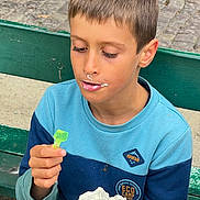 Jean a rejoint le concours — aidez-le/la à gagner de superbes lots ! child, boy, bench, whipped_cream, dessert, food, green_spoon, outdoor, casual_clothing, blue_sweater, face, expression, eating, close_up, daylight, park, young, person, nose, hand
