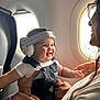 baby, headphones, smile, airplane, window, adult, holding, overalls, white_shirt, happy, child, seat, travel, person, glasses, light, inside, portrait, interaction, cute