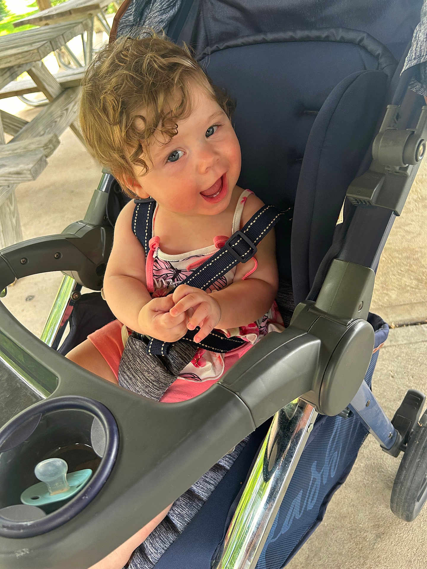 Iryis joined the competition — help win amazing prizes! toddler, child, stroller, curly_hair, smiling, happy, outdoor, picnic_table, seatbelt, summer_clothing, baby, person, playful, daylight, concrete_floor, plastic, metal, casual, cute, portrait