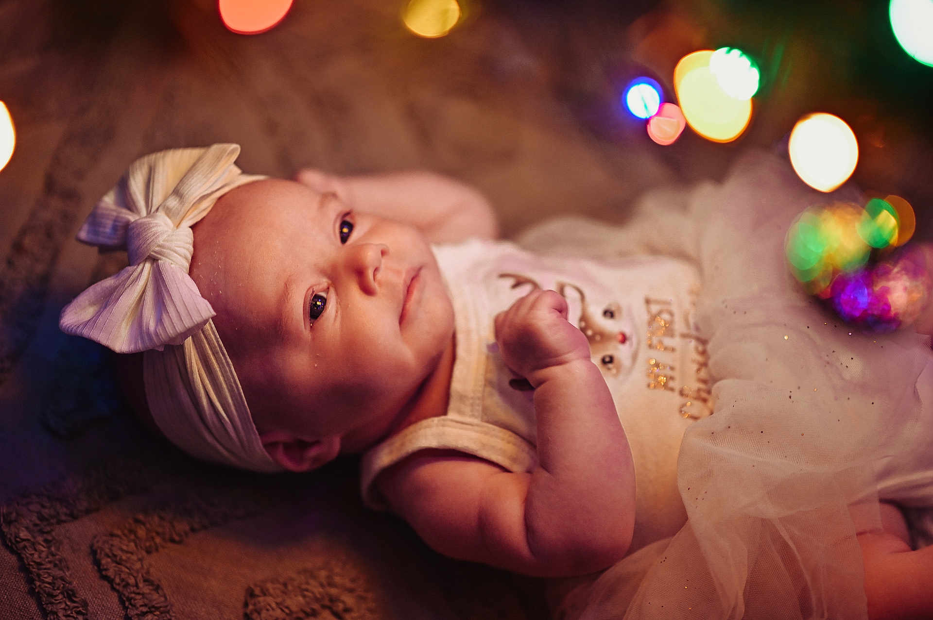 Maeve is registered to the contest to win money with this photo: baby, infant, headband, bow, blanket, tutu, bokeh, lights, portrait, cute, soft_lighting, sleepy, child, newborn, face, hand, lying_down, clothing, indoors, decorative