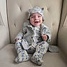 adorable, baby, baby_suit, cardigan, chair, child, close_up, clothing, furniture, happy, hat, indoor, infant, patterned_outfit, photography, portrait, sitting, smiling, socks, tufted_chair