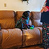 adult, black_dog, christmas_wreath, couch, dog, festive_clothing, furniture, holiday_decor, holiday_pajamas, indoor, living_room, man, pajamas, pet, pet_clothing, pointing, quilted_couch_cover, toy_ball, wall_decor, wood_floor