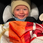 Atlas is registered to the contest to win money with this photo: baby, smiling, hat, blanket, cozy, child, infant, cute, warm, seated, portrait, face, clothing, closeup, indoors, comfort, headwear, happy, person, baby_carrier