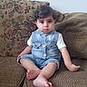 baby, barefoot, brown_hair, child, couch, denim, face, fashion, floral, furniture, home, indoor, overalls, photography, portrait, serious, shirt, sitting, sofa, toddler