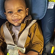 Robert is registered to the contest to win money with this photo: toddler, child, smiling, car_seat, pacifier, brown_jacket, seatbelt, indoor, cute, baby, happy, face, clothing, sitting, closeup, infant, person, young_child, secure, toy