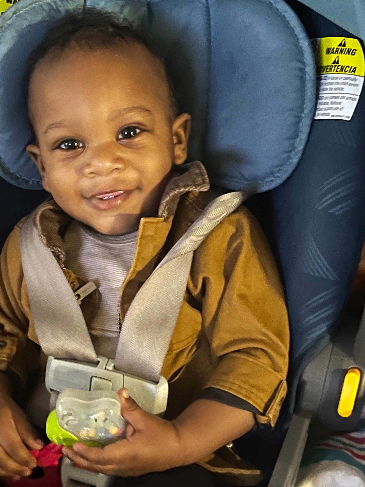 Robert is registered to the contest to win money with this photo: toddler, child, smiling, car_seat, pacifier, brown_jacket, seatbelt, indoor, cute, baby, happy, face, clothing, sitting, closeup, infant, person, young_child, secure, toy