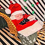 baby, sleeping, santa_hat, christmas_outfit, woven_sleigh, blanket, holiday, festive, red_clothing, black_bow, white_fur_trim, background_stripes, decorative_bows, newborn, cozy, cute, portrait, indoor, celebration, seasonal