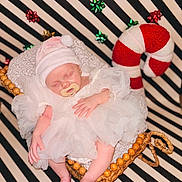 Presley joined the competition — help win amazing prizes! baby, sleeping, white_dress, pink_hat, pacifier, wicker_cradle, striped_background, decorative_bows, candy_cane, holiday_theme, infant, cozy, soft_lighting, portrait, festive, cute, resting, newborn, indoor, decor
