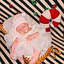 baby, sleeping, white_dress, pink_hat, pacifier, wicker_cradle, striped_background, decorative_bows, candy_cane, holiday_theme, infant, cozy, soft_lighting, portrait, festive, cute, resting, newborn, indoor, decor