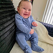 Yusef joined the competition — help win amazing prizes! baby, infant, smiling, blue_onesie, couch, blanket, cozy, chubby_cheeks, indoor, portrait, sitting, calendar, bookshelf, vertical_blinds, natural_light, happy, hand, foot, furniture, soft_texture