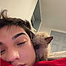 cat, person, sleeping, sleepy, cuddling, portrait, close_up, indoors, bedroom, blanket, red_blanket, fluffy, pet, companion, face, relaxed, cozy, home, selfie, nap