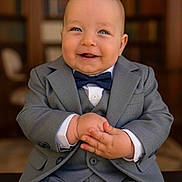 Matéo a rejoint le concours — aidez-le/la à gagner de superbes lots ! baby, child, suit, bow_tie, smile, happy, portrait, indoor, formal_wear, hands, face, blue_eyes, seated, candid, cute, toddler, person, clothing, fashion, background