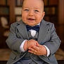 Matéo participe au concours pour gagner de l'argent avec cette photo : baby, child, suit, bow_tie, smile, happy, portrait, indoor, formal_wear, hands, face, blue_eyes, seated, candid, cute, toddler, person, clothing, fashion, background