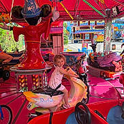 Milana participe au concours pour gagner de l'argent avec cette photo : child, carousel, amusement_ride, toy_scooter, barbie, bright_colors, mickey_mouse, wizard_hat, lights, funfair, outdoor, playful, happy, curly_hair, pink_floor, ride, entertainment, smiling, person, daytime
