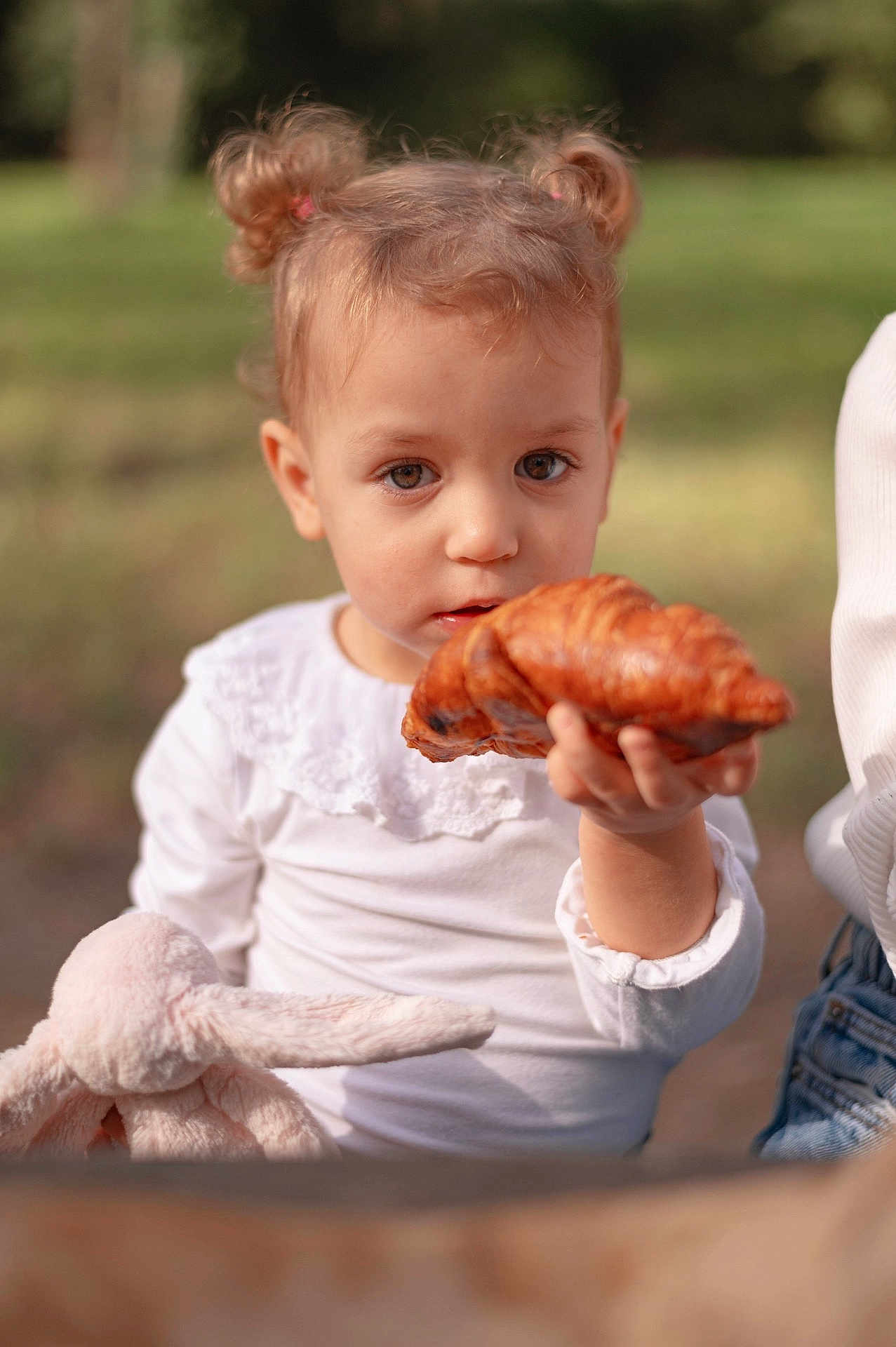 Milana a rejoint le concours — aidez-le/la à gagner de superbes lots ! child, toddler, croissant, bread, stuffed_animal, bunny, toy, white_clothing, outdoor, greenery, face, portrait, hair_buns, curly_hair, holding, food, nature, daylight, cute, person