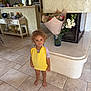 Milana participe au concours pour gagner de l'argent avec cette photo : child, toddler, barefoot, curly_hair, yellow_towel, indoor, tile_floor, fireplace, flowers, vase, cabinet, decor, smile, purple_shirt, home, living_room, plant, furniture, cute, portrait