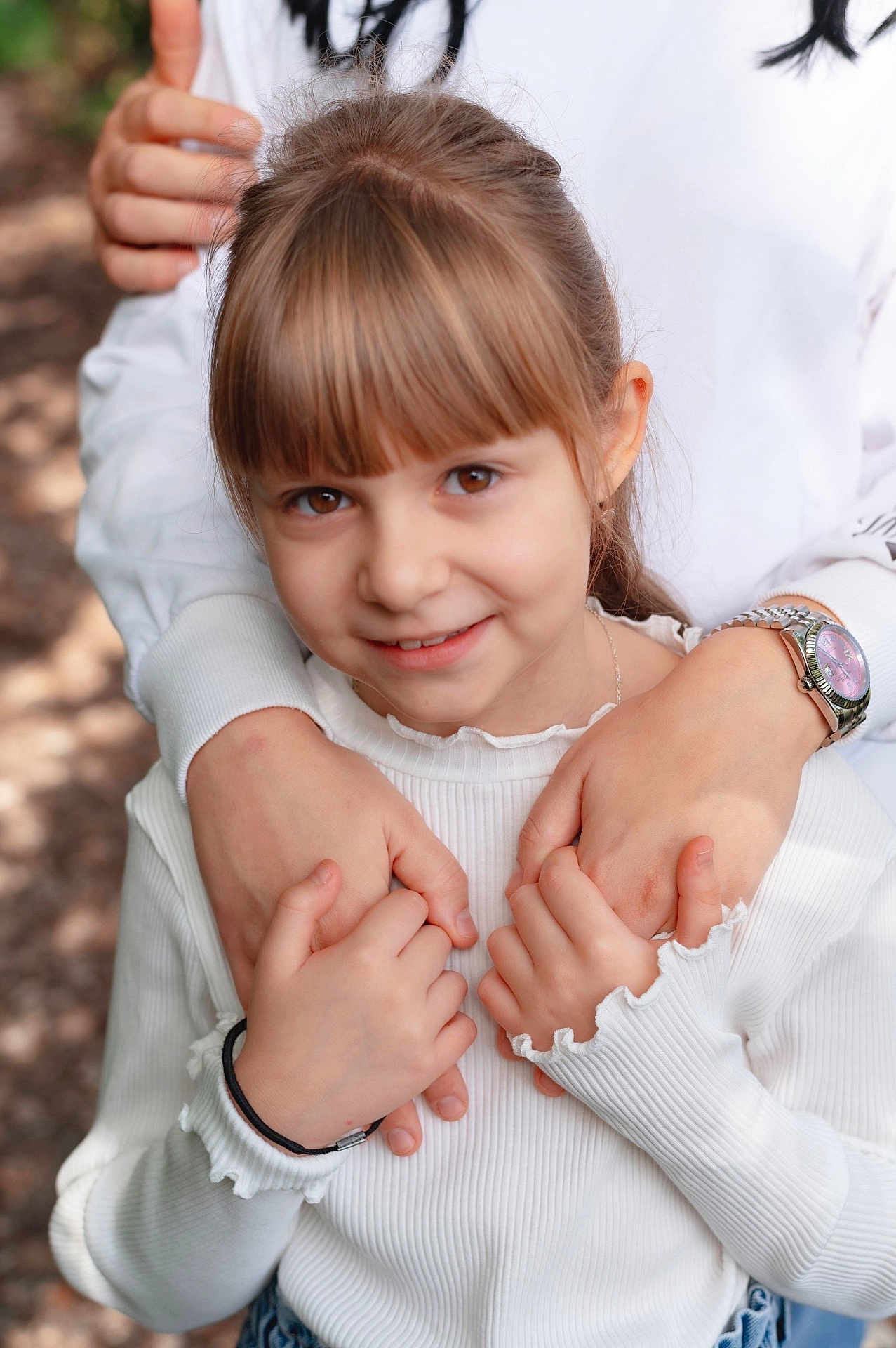 Anastasia participe au concours pour gagner de l'argent avec cette photo : child, girl, smile, hands, embrace, white_sweater, watch, bracelet, outdoor, portrait, brown_eyes, long_hair, fringe, happy, affection, family, love, casual_clothing, natural_light, closeup