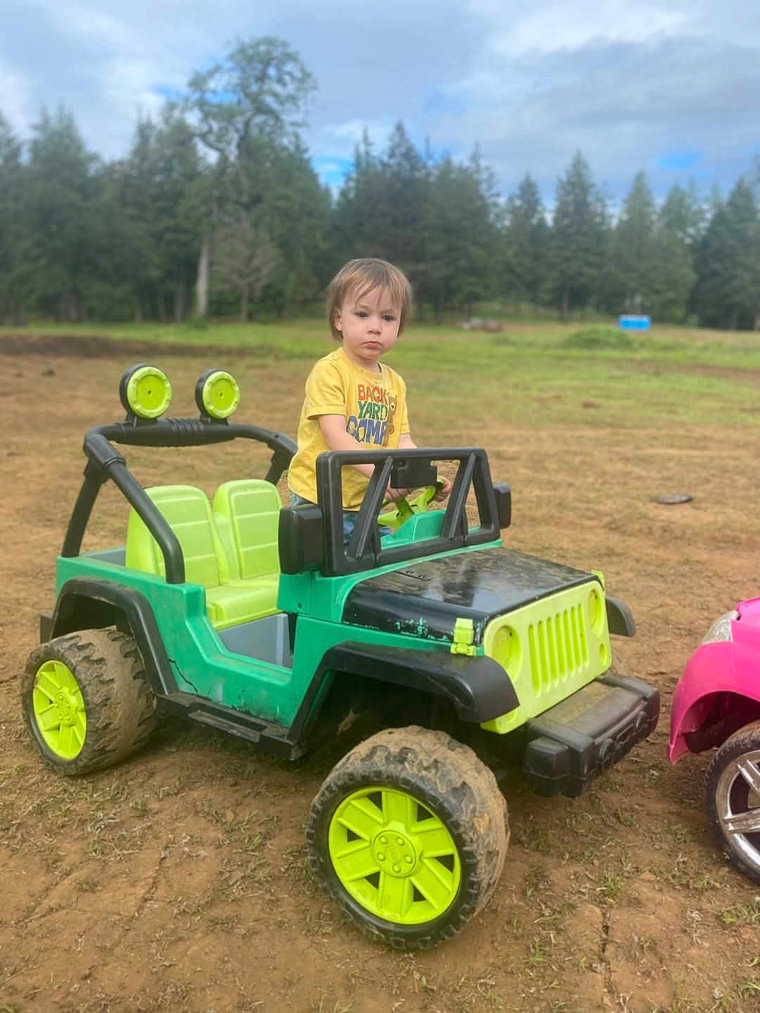 Ryker joined the competition — help win amazing prizes! child, toddler, toy_car, jeep, outdoor, muddy, grass, dirt, yellow_shirt, green, play, vehicle, nature, trees, sky, cloudy, wheels, park, serious, boy