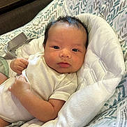 Eric is registered to the contest to win money with this photo: baby, infant, face, person, cushion, seat, clothing, white, skin, arm, head, indoor, expression, young, human, newborn, cute, portrait, resting, comfort