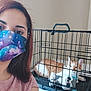 Milky is registered to the contest to win money with this photo: woman, face_mask, cat, pet_crate, plush_toy, orange_cat, white_cat, indoor, portrait, pet, furniture, cage, resting_cat, person, casual_clothing, short_hair, table, metal_bars, looking_at_camera, animal