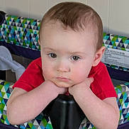 Harold is registered to the contest to win money with this photo: baby, child, infant, playpen, red_shirt, face, arms, indoor, patterned_fabric, geometric_pattern, expressionless, resting, closeup, skin, hair, person, young_child, furniture, head, portrait