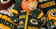 Quincy is registered to the contest to win money with this photo: baby, infant, newborn, pacifier, football, sports_fan, green_bay_packers, team_jersey, beanie, mittens, blanket, portrait, lying_down, indoors, cozy, colorful, green_and_gold, sports_merchandise, smiling, close_up