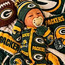 baby, beanie, blanket, close_up, colorful, cozy, football, green_and_gold, green_bay_packers, indoors, infant, lying_down, mittens, newborn, pacifier, portrait, smiling, sports_fan, sports_merchandise, team_jersey