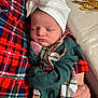 baby, newborn, sleeping, plaid, red, green, white_bow, hat, hand, cozy, fabric, person, indoor, close_up, infant, soft_skin, peaceful, wrapped, holding, portrait