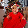 baby, child, red_dress, white_socks, headband, smile, christmas_tree, ornaments, tinsel, chair, wooden_chair, holiday, festive, indoor, decorations, gifts, floor_tiles, cabinet, mirror, happy