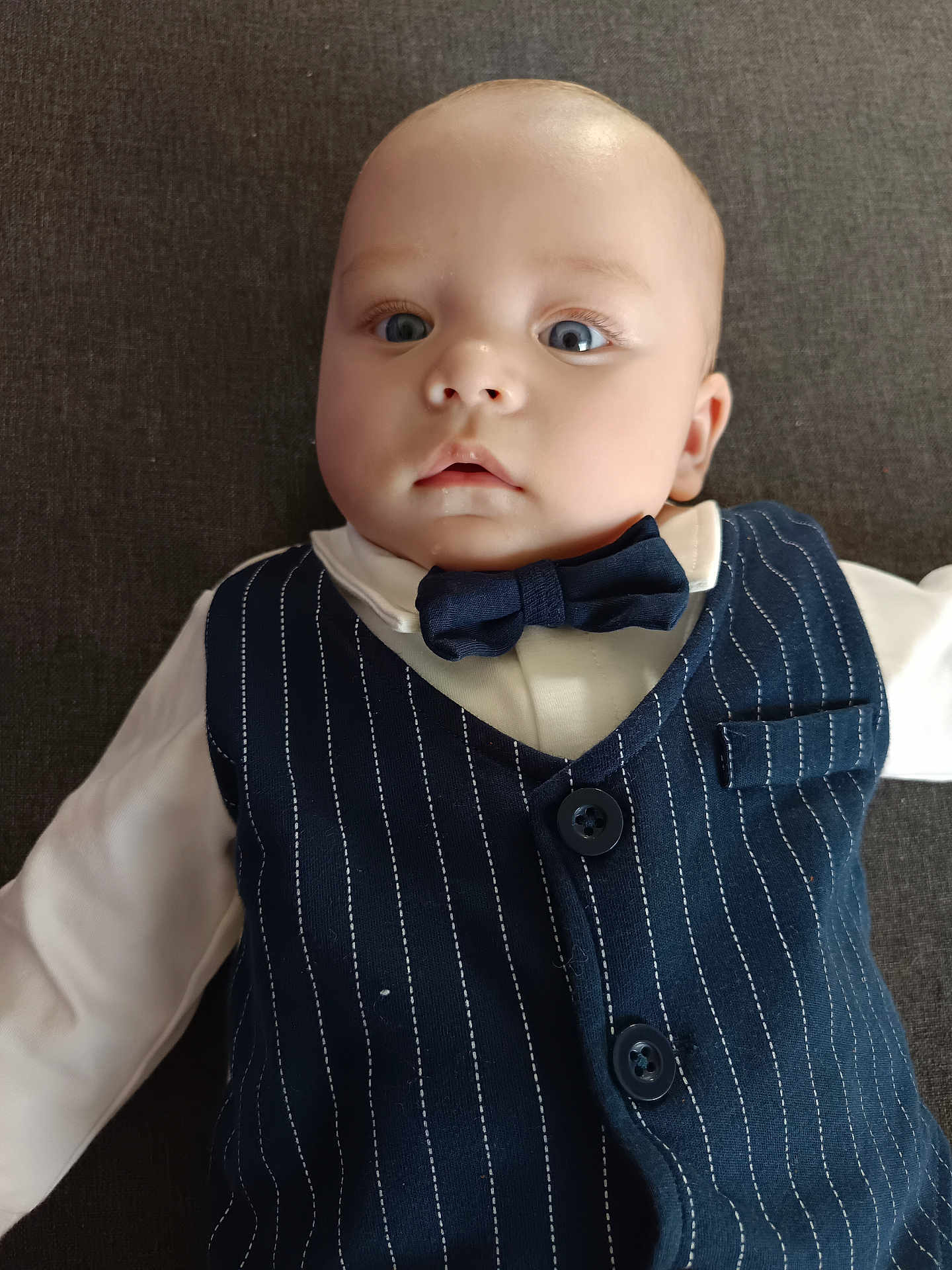 Lylio participe au concours pour gagner de l'argent avec cette photo : baby, infant, child, face, blue_eyes, bow_tie, vest, pinstripe, white_shirt, clothing, portrait, lying_down, cute, young, person, indoors, fashion, formal, expression, head