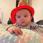 Ethan a rejoint le concours — aidez-le/la à gagner de superbes lots ! baby, child, fire_chief_hat, red_hat, blanket, indoor, person, hand, curious, soft_texture, blonde_hair, adult, wall, light, reaching, cute, infant, young_child, portrait, cozy