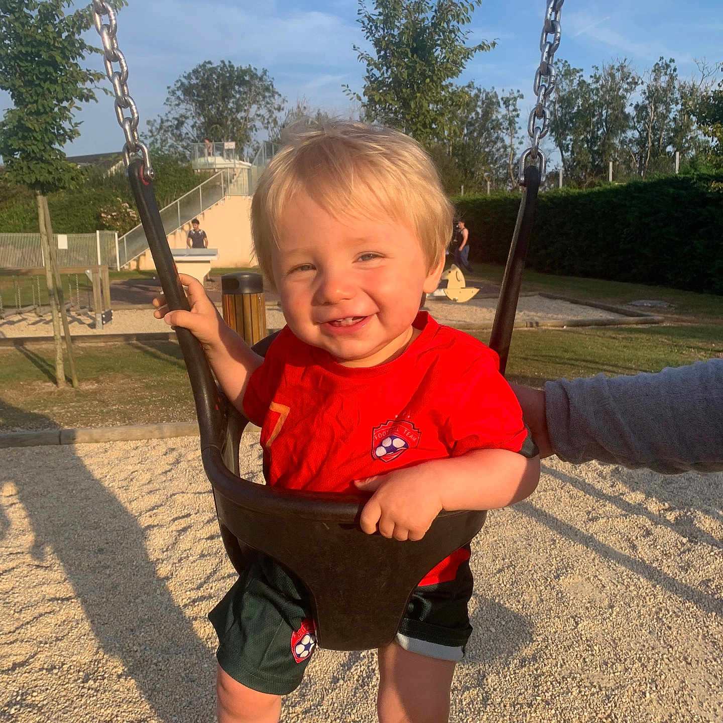 Ayden participe au concours pour gagner de l'argent avec cette photo : barefoot, chain, child, daylight, fun, grass, happy, outdoor, park, person, play, playground, red_shirt, shorts, smiling, sunny, supporting_hand, swing, toddler, trees