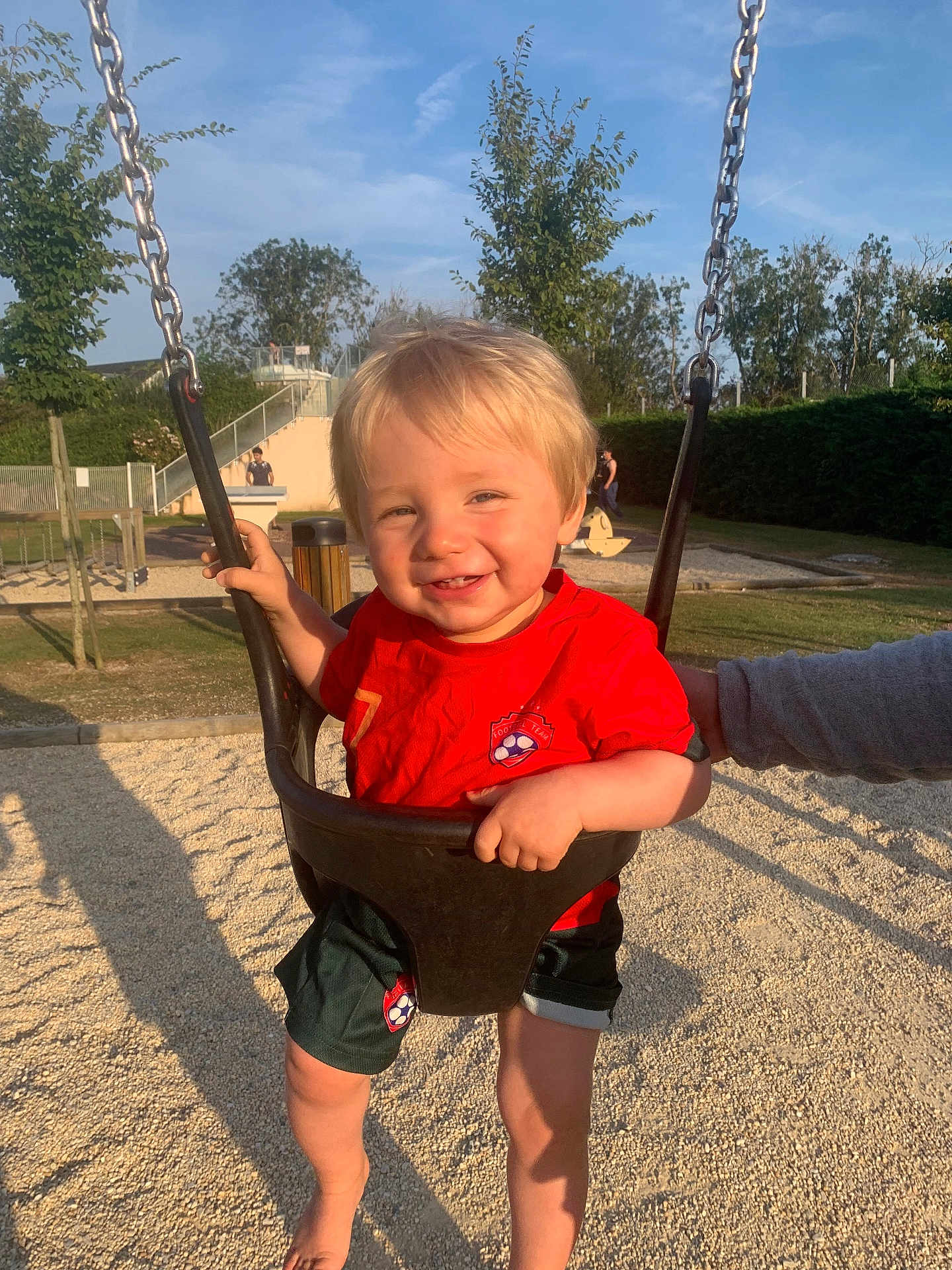 Ayden participe au concours pour gagner de l'argent avec cette photo : barefoot, chain, child, daylight, fun, grass, happy, outdoor, park, person, play, playground, red_shirt, shorts, smiling, sunny, supporting_hand, swing, toddler, trees