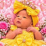 Noa is registered to the contest to win money with this photo: baby, infant, child, portrait, face, eyes, yellow_dress, bow, tiara, crown, flowers, roses, daisies, pink_background, hearts, festive, costume, lying_down, floral_decoration, photography