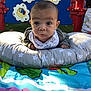 baby, child, outdoor, playground, pillow, colorful, curious_expression, clothing, play_mat, face, person, toddler, green, blue, red, yellow, fabric, head, smile, infant