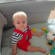 Mael participe au concours pour gagner de l'argent avec cette photo : baby, blonde_hair, child, couch, curious, cute, floor, footwear_free, indoor, light_hair, play_mat, polka_dots, red_overalls, sitting, smile, soft_furniture, striped_shirt, toddler, toys, young_child