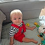 baby, blonde_hair, child, couch, curious, cute, floor, footwear_free, indoor, light_hair, play_mat, polka_dots, red_overalls, sitting, smile, soft_furniture, striped_shirt, toddler, toys, young_child