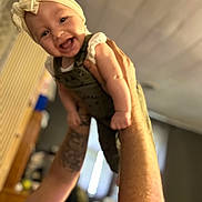 Raelynn joined the competition — help win amazing prizes! baby, child, smiling, headband, bow, arms, tattoo, indoor, person, happy, lifting, cute, infant, clothing, portrait, face, skin, background, blur, warm_light