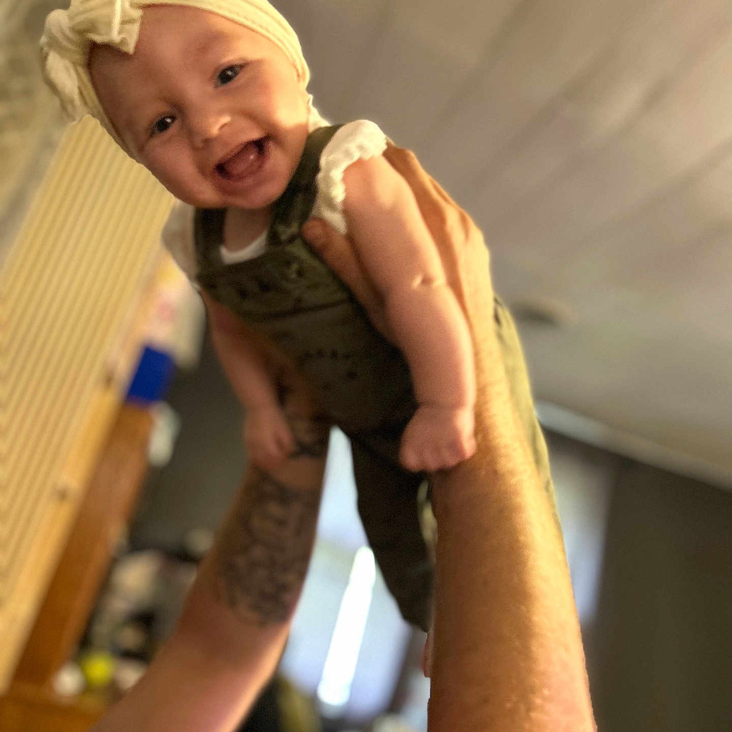 Raelynn joined the competition — help win amazing prizes! arms, baby, background, blur, bow, child, clothing, cute, face, happy, headband, indoor, infant, lifting, person, portrait, skin, smiling, tattoo, warm_light