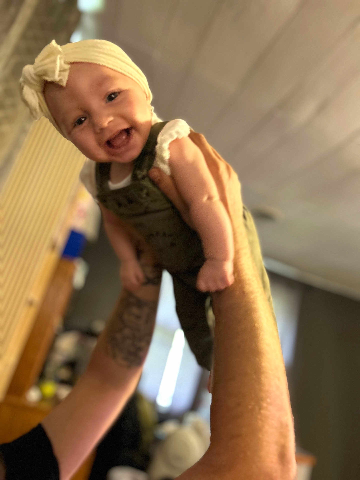 Raelynn joined the competition — help win amazing prizes! baby, child, smiling, headband, bow, arms, tattoo, indoor, person, happy, lifting, cute, infant, clothing, portrait, face, skin, background, blur, warm_light