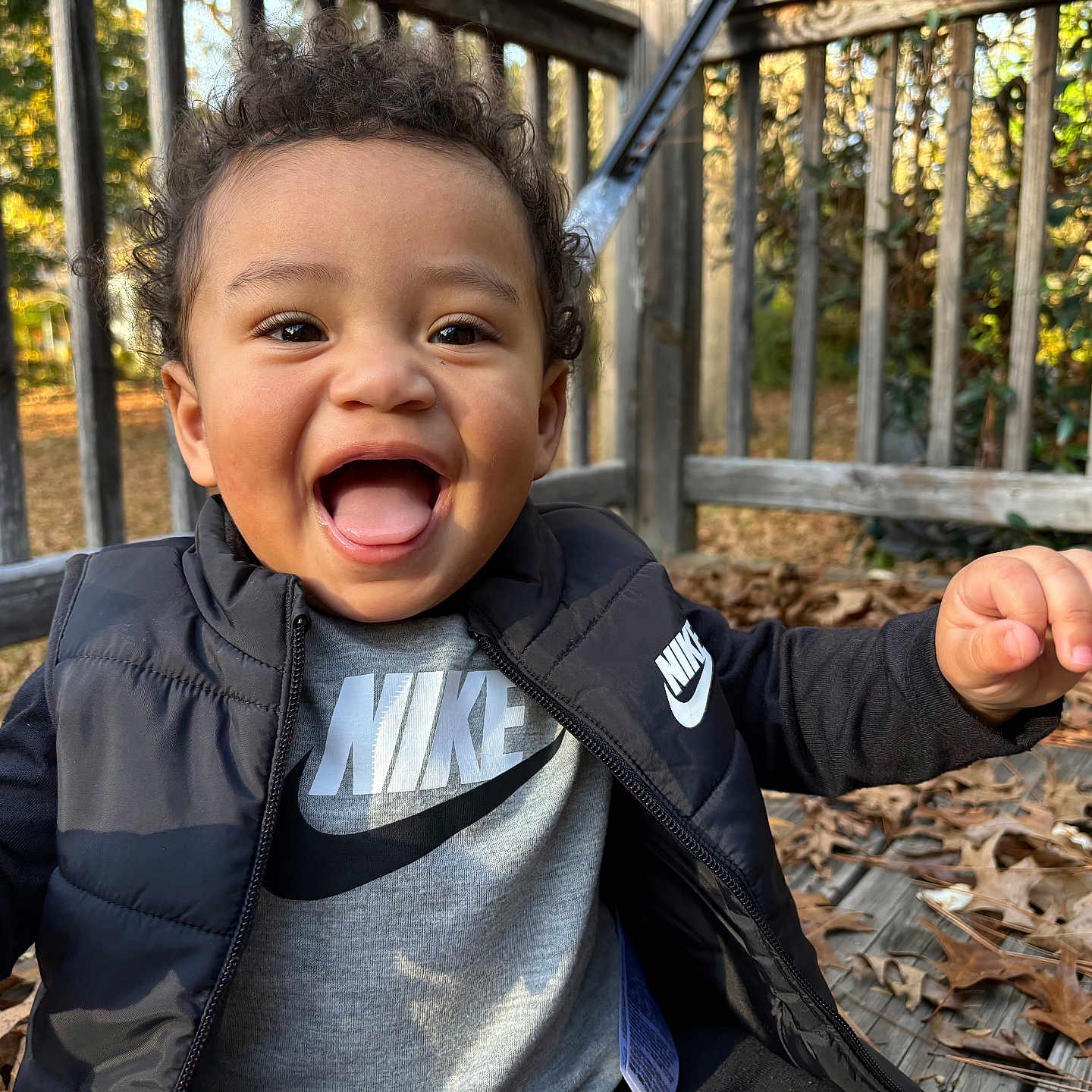 Eliyah is registered to the contest to win money with this photo: baby, bodypart, clothing, coat, face, fence, finger, grass, hand, happy, head, jacket, laughing, outdoors, pants, person, photography, plant, portrait, tree