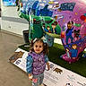 child, girl, pigtails, purple_vest, jeans, white_shoes, bandage, bear_sculpture, colorful_art, cartoon_characters, indoor, plant, signage, floor, museum, smiling, standing, hair_bows, public_space, leeds_hospitals_charity