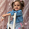 child, girl, pigtails, tiara, blue_sweater, cartoon, jeans, patches, white_chair, smile, happy, indoor, portrait, cute, sparkles, pink_background, seated, young, fashion, playful