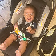Zachariah is registered to the contest to win money with this photo: baby, car_seat, smiling, happy, infant, pacifier, snack_pouch, legs, feet, clothing, indoor, floor, bag, tiled_floor, child, person, seatbelt, cute, expression, holding