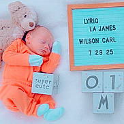 Lyriq joined the competition — help win amazing prizes! newborn, baby, sleeping, teddy_bear, orange_outfit, mittens, booties, letter_board, blocks, name_board, soft_blanket, cute, infant, portrait, resting, child, indoors, baby_clothes, peaceful, toy