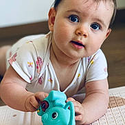 Romy a rejoint le concours — aidez-le/la à gagner de superbes lots ! baby, child, toy, blue_toy, elephant_toy, floor, infant, cute, curious, lying_down, white_clothing, butterfly_pattern, hand, face, big_eyes, indoor, wooden_floor, young_child, person, portrait