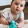 baby, child, toy, blue_toy, elephant_toy, floor, infant, cute, curious, lying_down, white_clothing, butterfly_pattern, hand, face, big_eyes, indoor, wooden_floor, young_child, person, portrait