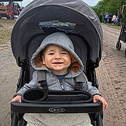 Brooks Bennett is registered to the contest to win money with this photo: toddler, child, stroller, hoodie, blanket, smile, outdoor, path, trees, people, graco, happy, baby, person, casual_clothing, daytime, nature, park, family, transport